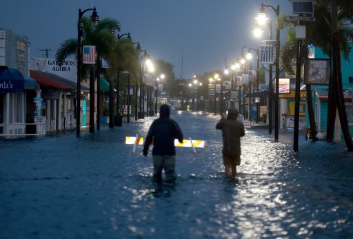 Reporters wade through flood waters as it inundates the down